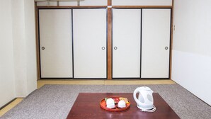 Una habitación con suelo de estera de tatami, una mesa de madera con una bandeja de comida y una tetera, y una puerta corredera con aire acondicionado instalado en el techo.
