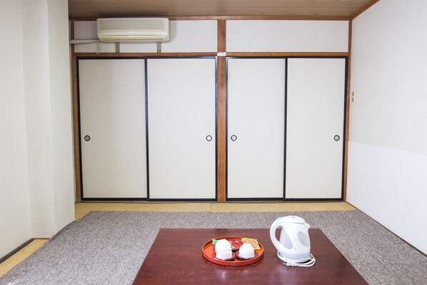 Una habitación con suelo de estera de tatami, una mesa de madera con una bandeja de comida y una tetera, y una puerta corredera con aire acondicionado instalado en el techo.