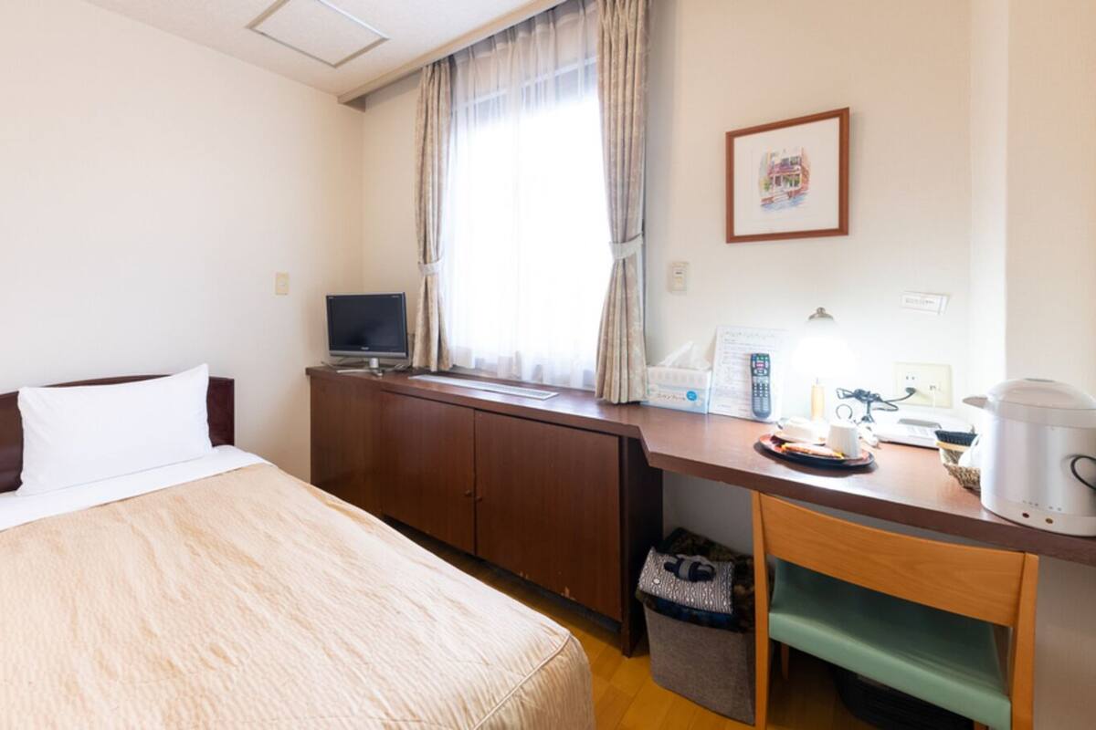Habitación de hotel con cama, escritorio con computadora, cafetera y ventana con cortinas.