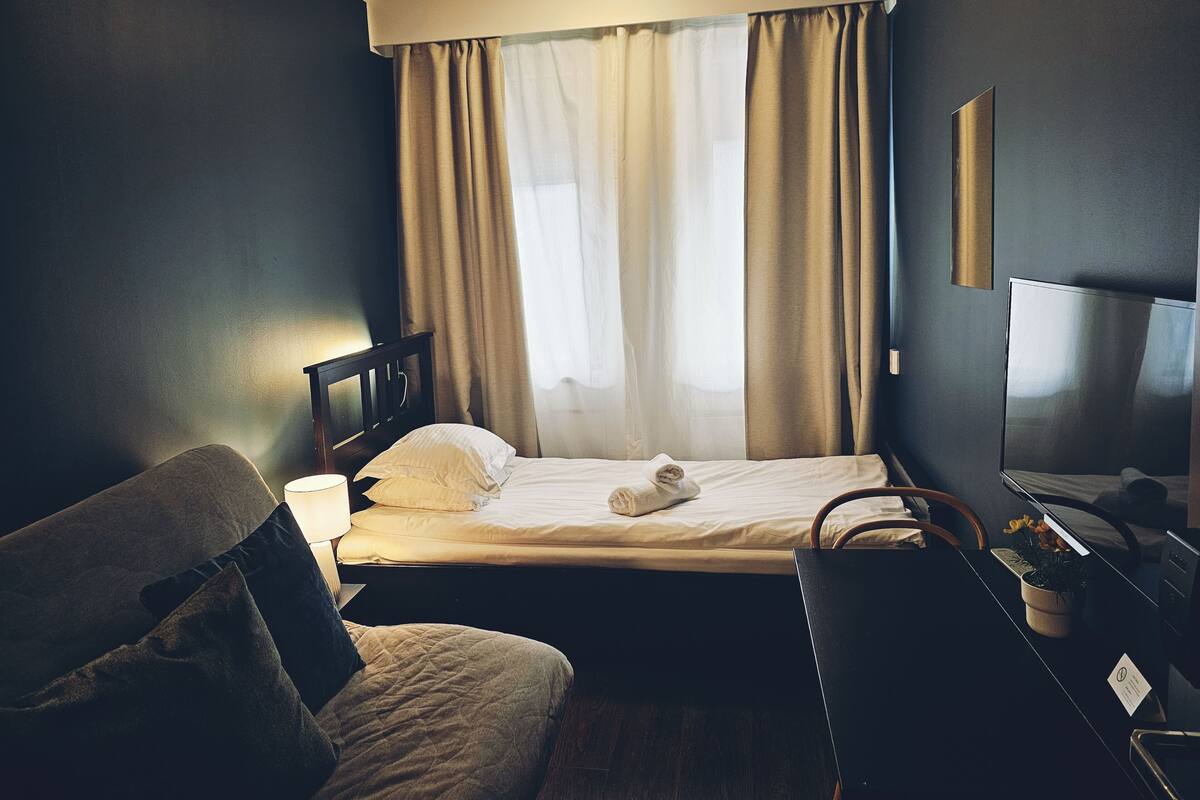 A hotel room with a bed, a chair, a desk, a TV, and a window with curtains.
