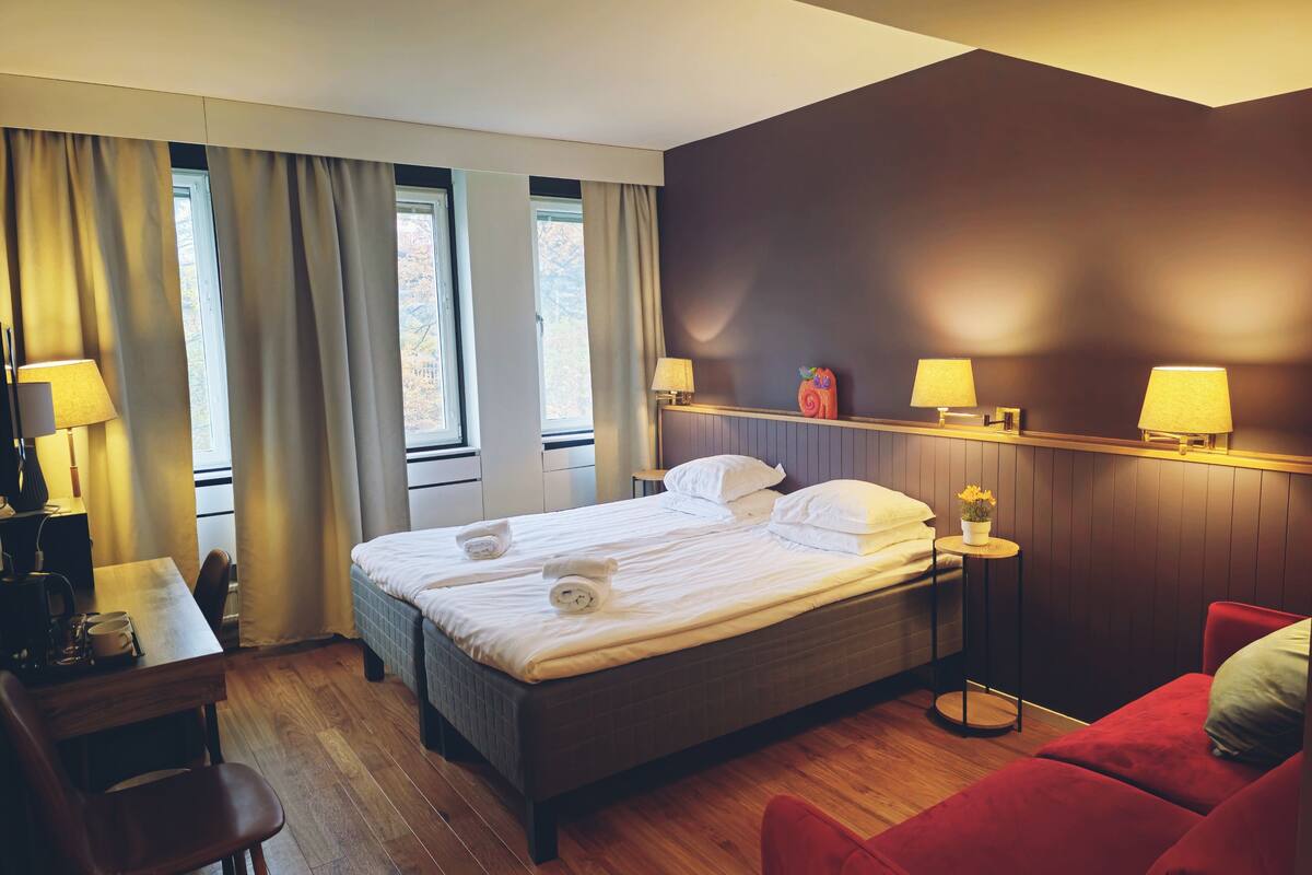 A hotel room with a large bed, a desk with a chair, a red sofa, and two bedside lamps.