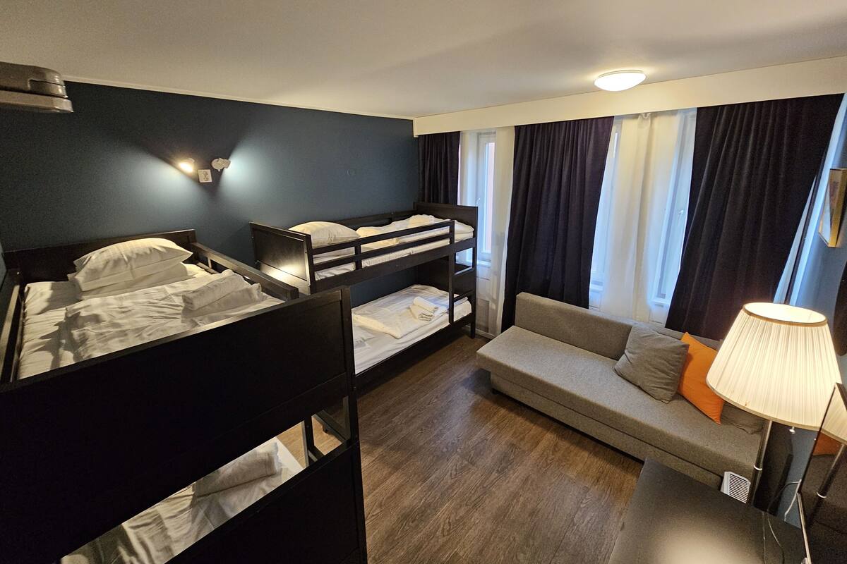 A room with bunk beds, a sofa, a lamp, and a window with curtains.