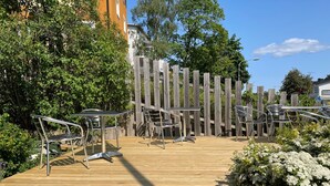 A wooden deck with metal chairs and a table, surrounded by greenery and a wooden fence. -  Lidingö Arena Hotel (Lidingo)