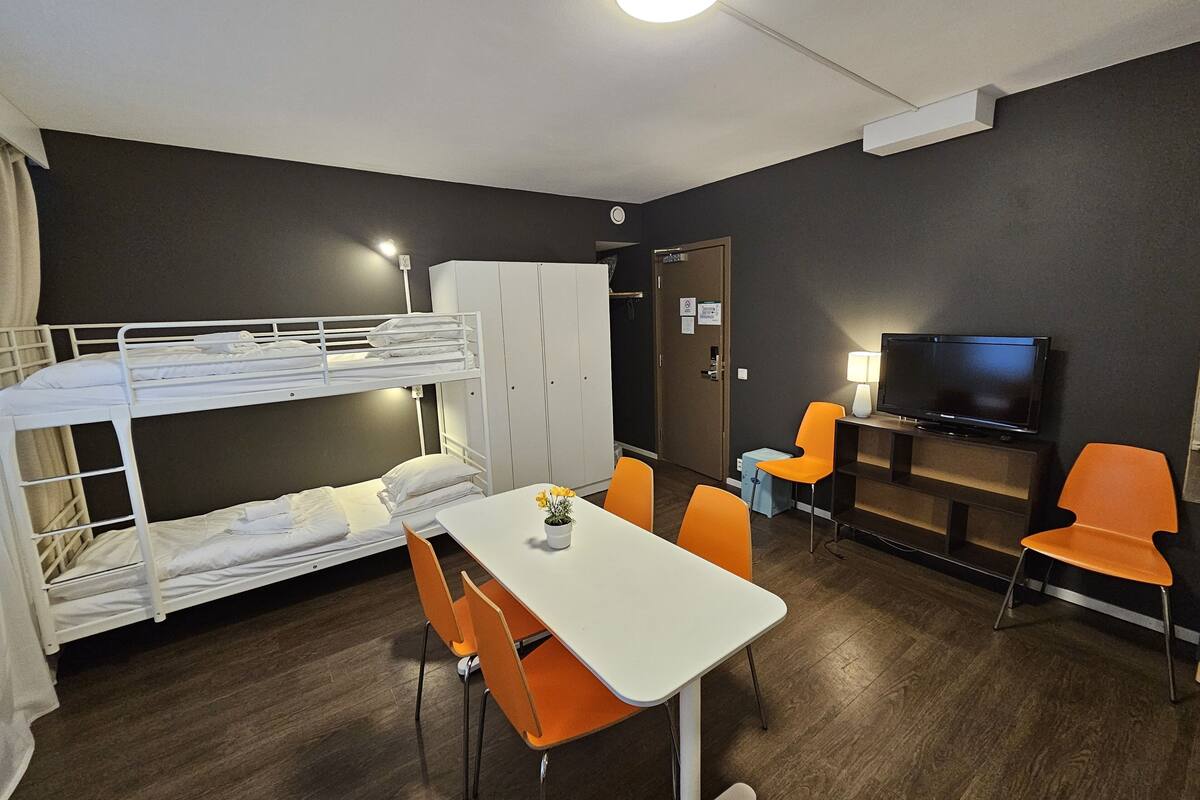 A bunk bed room with a table and chairs, a television, and a wardrobe.