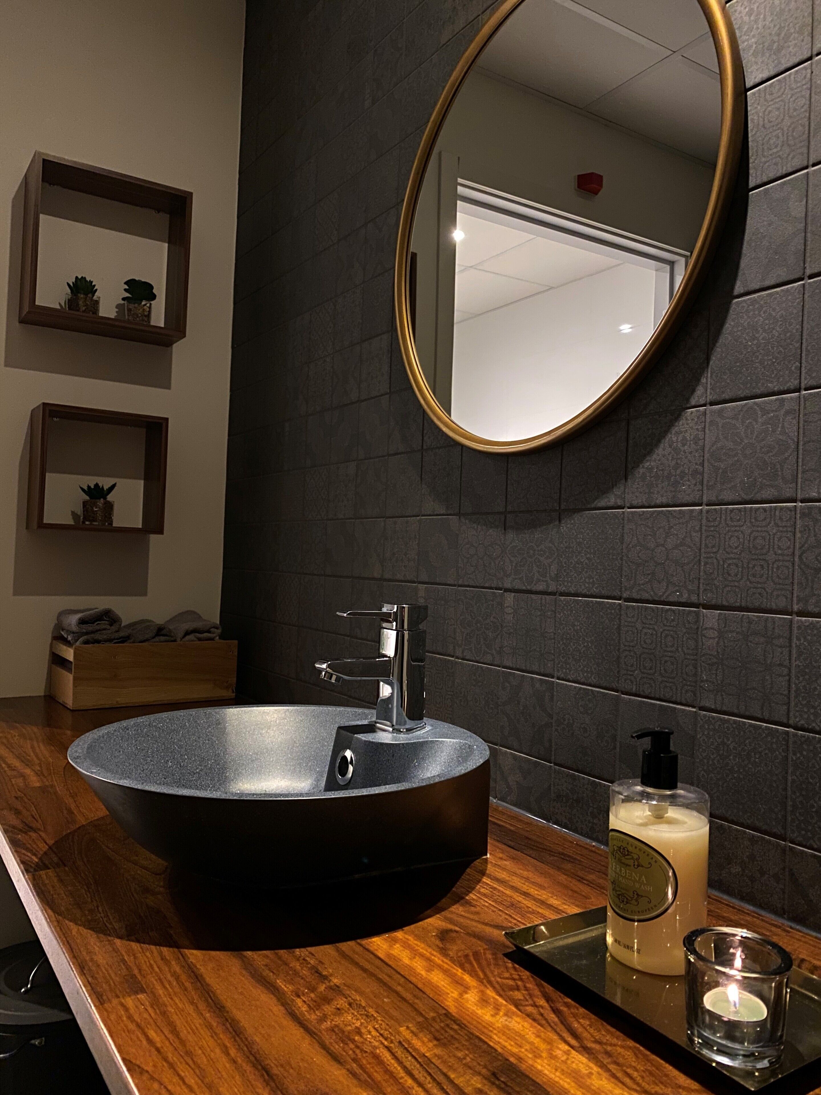 Un baño moderno con un lavamanos redondo negro, un espejo con marco dorado y un mueble de tocador de madera.