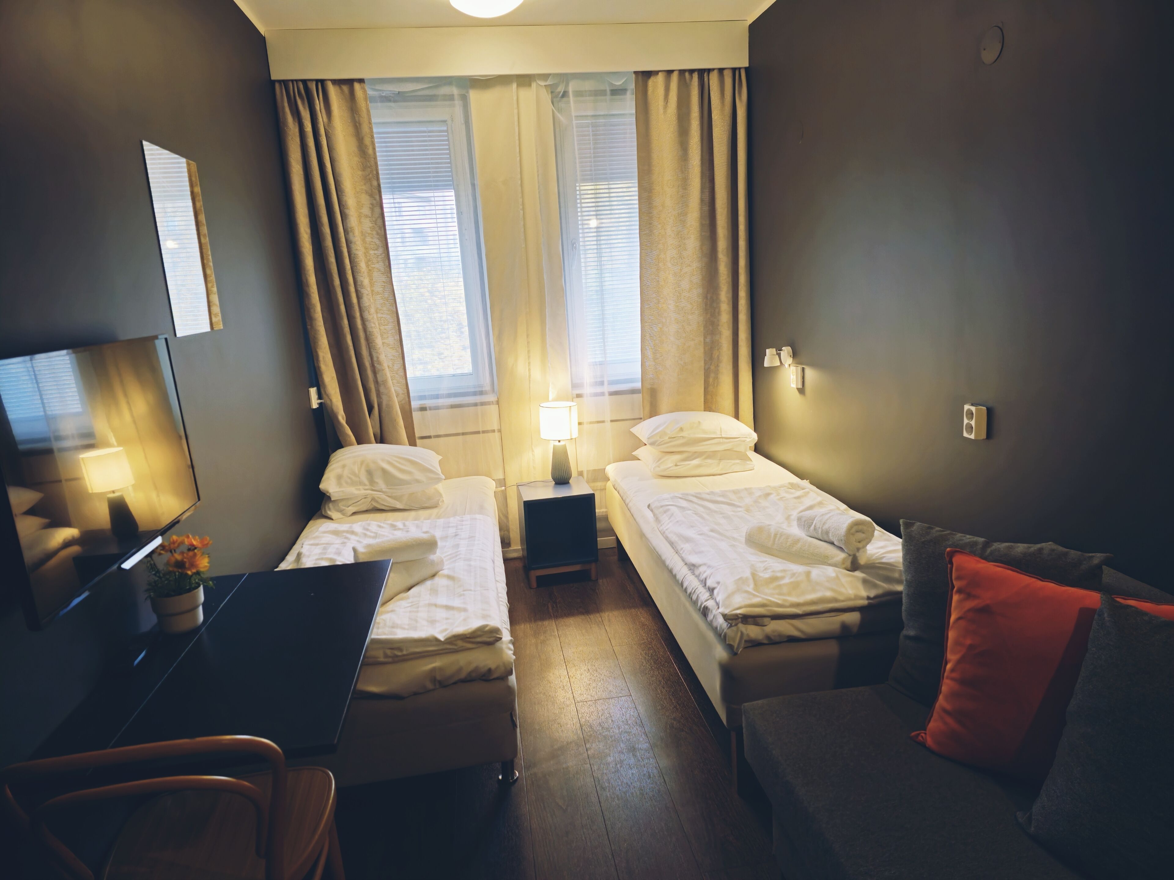 A hotel room with two beds, a desk, a chair, a TV, and a window with curtains.