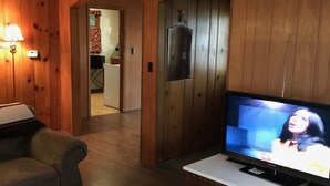 Una sala de estar con paredes de madera, un televisor sobre un mueble, un sofá y un ventilador de techo.