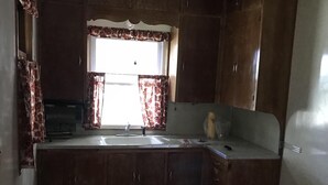 Una cocina compacta con armarios de madera, una ventana con cortinas florales y un lavabo.