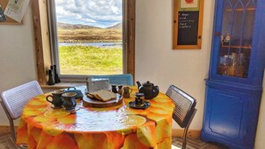 Une table à manger recouverte d’une nappe à motifs de fruits, avec une théière, un pichet et une assiette contenant du pain et du fromage.