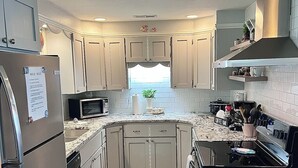 A kitchen with white cabinets, a stainless steel refrigerator, a microwave, a stove, and a coffee bar. - Tenkiller Bluff House (Park Hill)