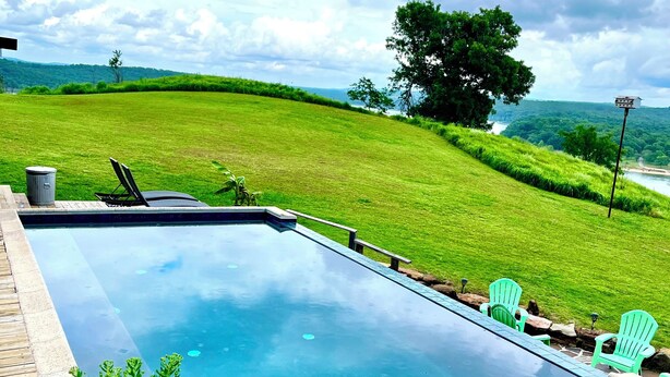 A swimming pool with a stone border, a wooden deck, and green chairs. - Tenkiller Bluff House (Park Hill)