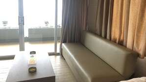 A room with a sofa, a table, and a sliding glass door leading to an outdoor area with plants. - St Paul Resort and Apartments (Safra)