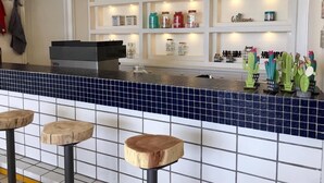 A bar area with a blue-tiled counter, wooden stools, and shelves with various items. - St Paul Resort and Apartments (Safra)