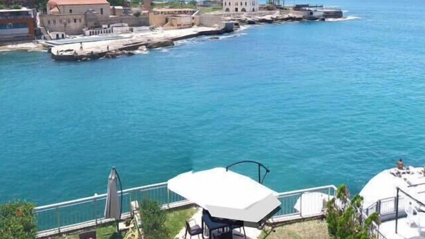 A coastal view with a patio area featuring a table and chairs, overlooking a body of water and buildings in the background. - St Paul Resort and Apartments (Safra)