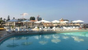 A pool area with white lounge chairs and umbrellas, a clear sky, and buildings in the background. - St Paul Resort and Apartments (Safra)
