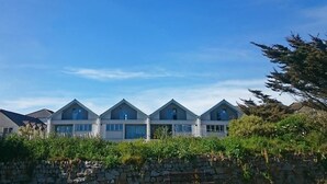 Une rangée de maisons modernes à plusieurs étages, dotées de grandes fenêtres et précédée d’un mur de pierre.
