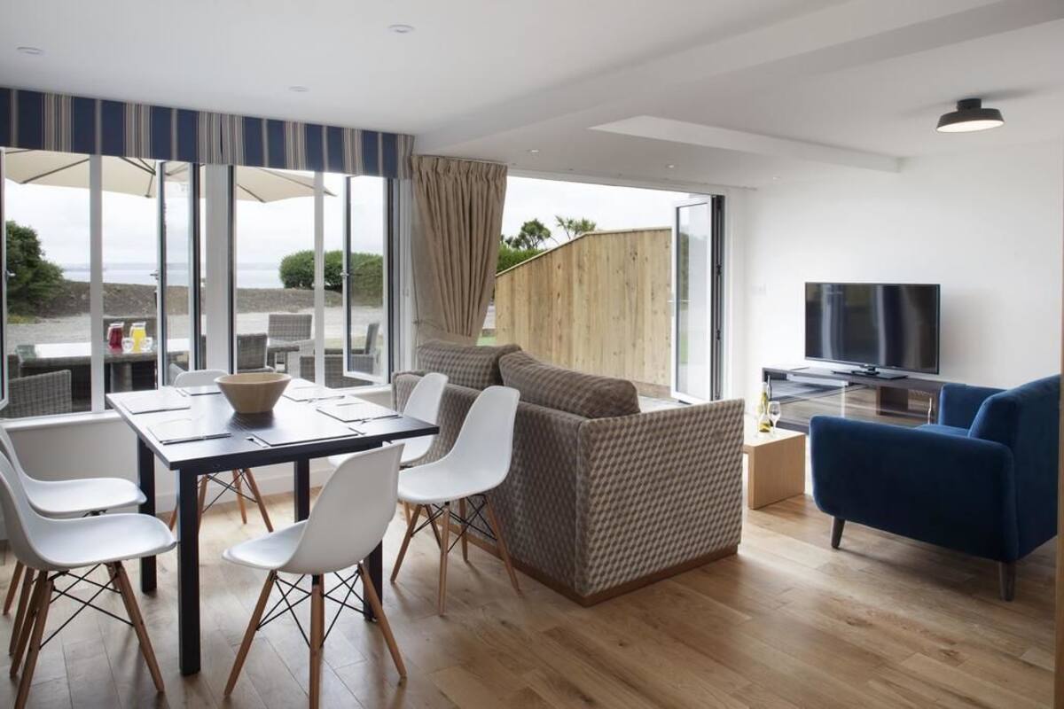 Een moderne woonkamer met een eethoek, een bank, een televisie en grote ramen.