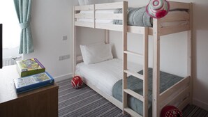 Une chambre avec un lit superposé, un bureau et une chaise, un radiateur et une fenêtre avec des rideaux.