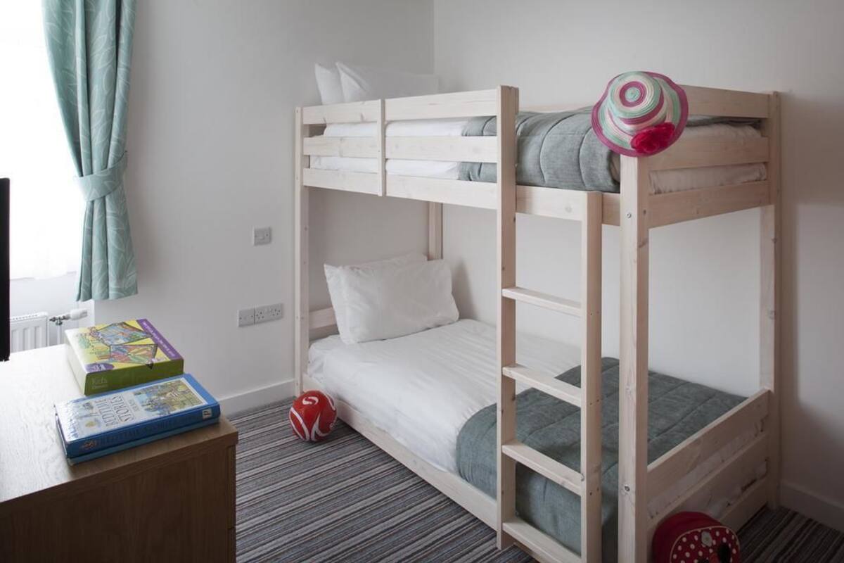 Een slaapkamer met een stapelbed, bureau en stoel, een radiator en een raam met gordijnen.