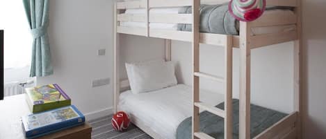 A bunk bed room with a desk and a chair, a radiator, and a window with curtains.