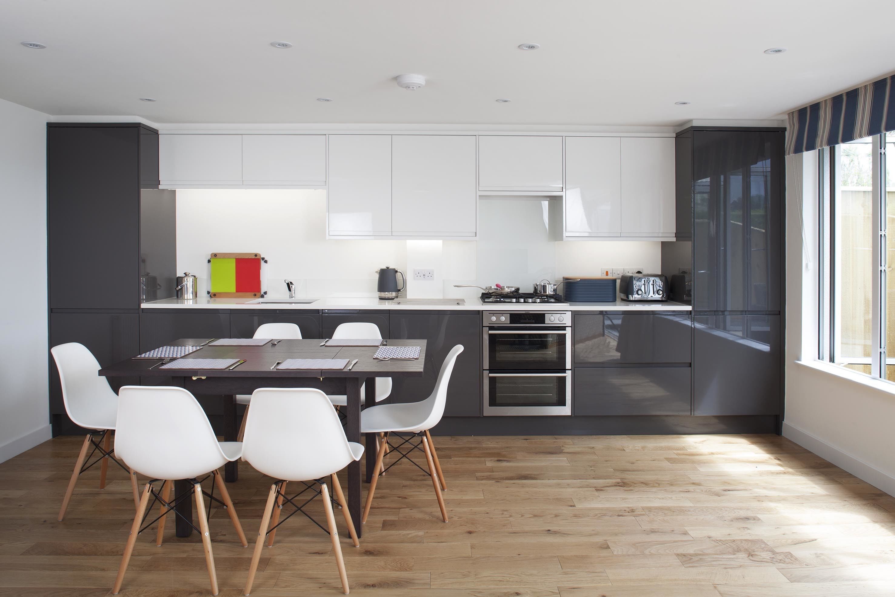 A modern kitchen with white cabinets, a dining table with white chairs, and a large window.