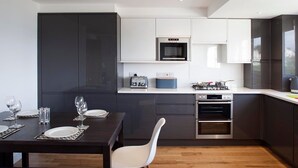 Une cuisine moderne avec des meubles de couleur sombre, un four encastré et un coin repas avec une table dressée pour deux personnes.