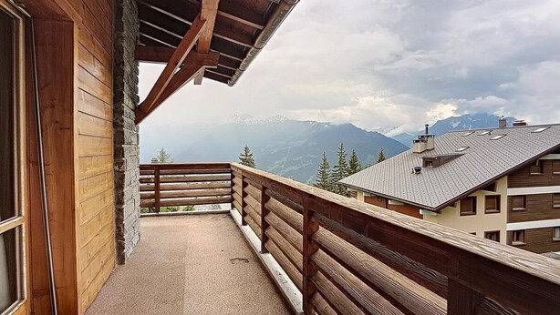 A wooden balcony with a view of mountains and a building in the background. - Vouamons A4 (Verbier)