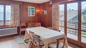 A dining area with a table and chairs, wooden walls, a radiator, and a view of the outside. - Vouamons A4 (Verbier)