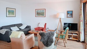 A living room with a sofa, armchairs, a coffee table, a TV, and framed pictures on the wall. - Vouamons A4 (Verbier)