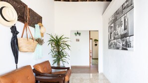 A hallway with a seating area featuring leather chairs, a potted plant, and wall-mounted items like a hat and a basket. - El Hostal Del Cubo (San Juan de la Rambla)