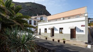 A building with a white facade, a balcony, and a mountain in the background. - El Hostal Del Cubo (San Juan de la Rambla)