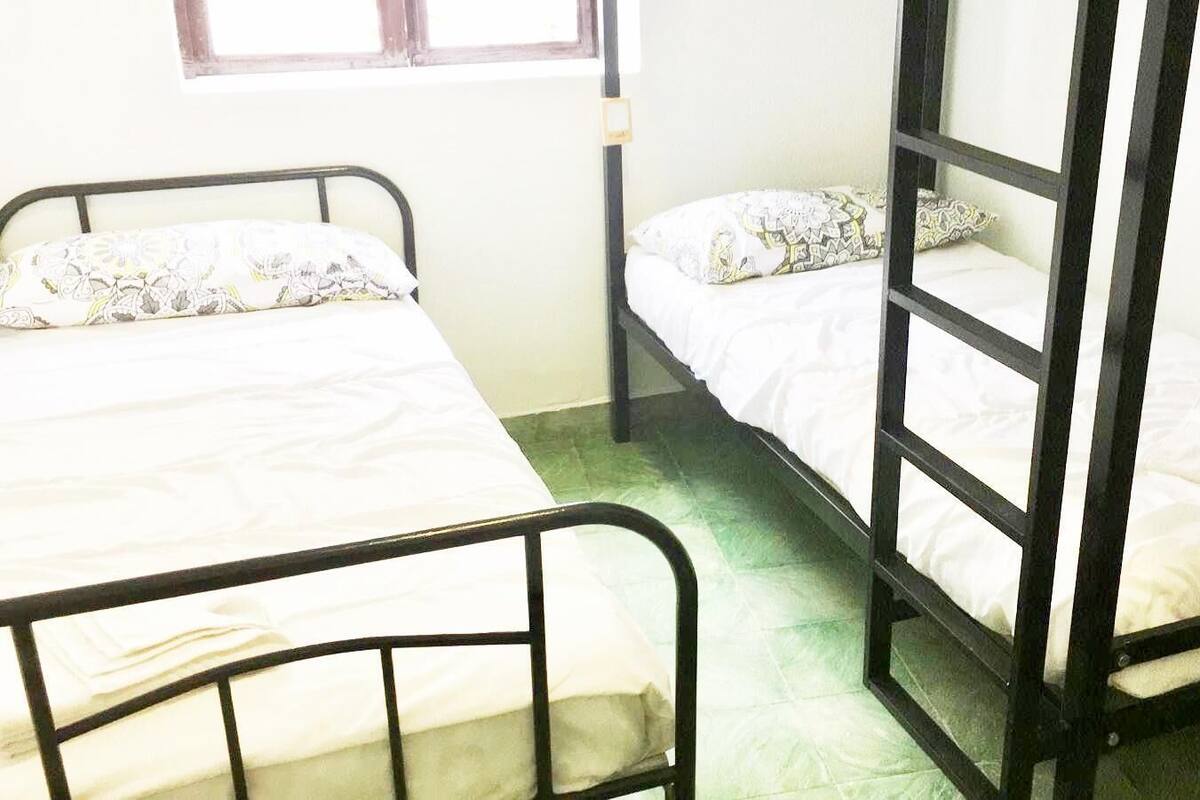 A dormitory room with two bunk beds, each with a patterned pillow and white bedding.