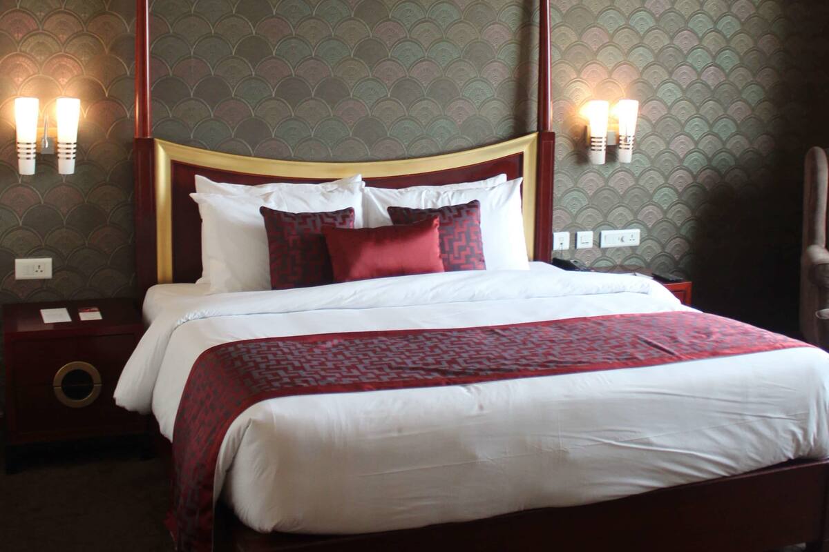 A neatly made bed with white and red bedding, a wooden headboard, and two wall-mounted light fixtures.