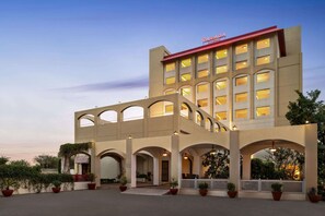 A hotel with a modern architectural design, featuring multiple balconies and a prominent entrance with a red awning. - Ramada by Wyndham Jaipur Jaisinghpura (Jaipur)