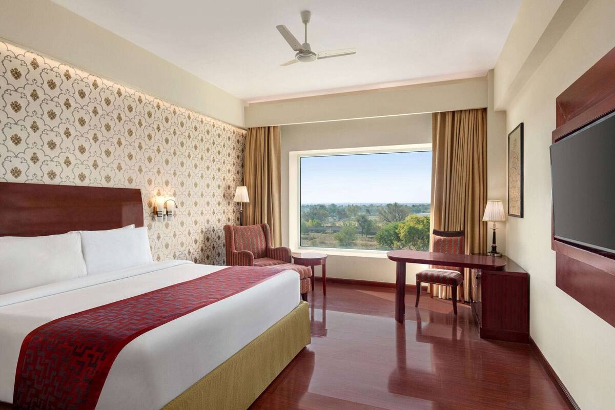 A hotel room with a large bed, a desk, a chair, a TV, and a view of the outdoors.