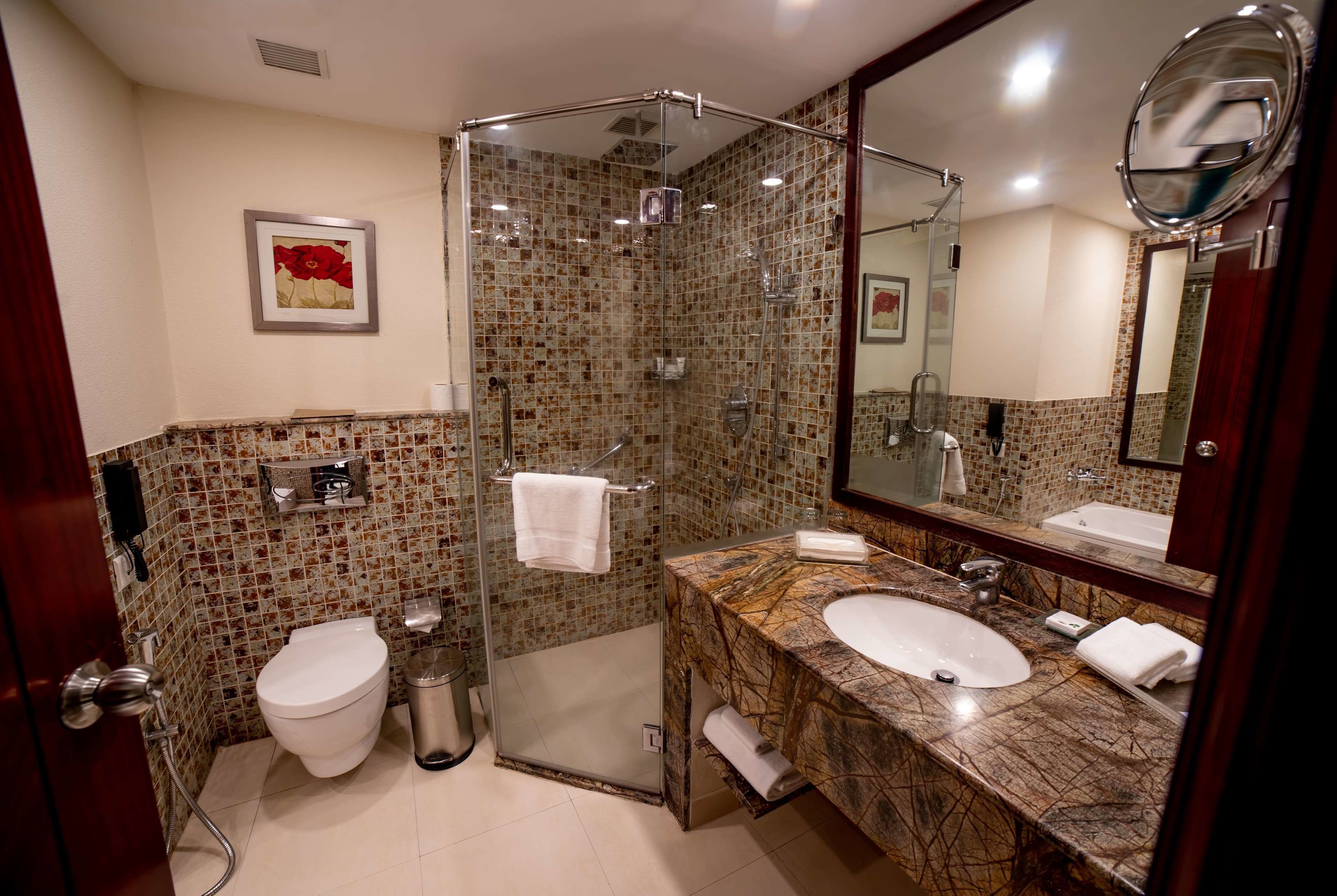 Un baño con ducha de vidrio, inodoro blanco, lavabo con encimera de mármol y un espejo grande.