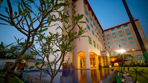 A hotel with a swimming pool, surrounded by greenery and a building with multiple windows and balconies. - Ramada by Wyndham Jaipur Jaisinghpura (Jaipur)