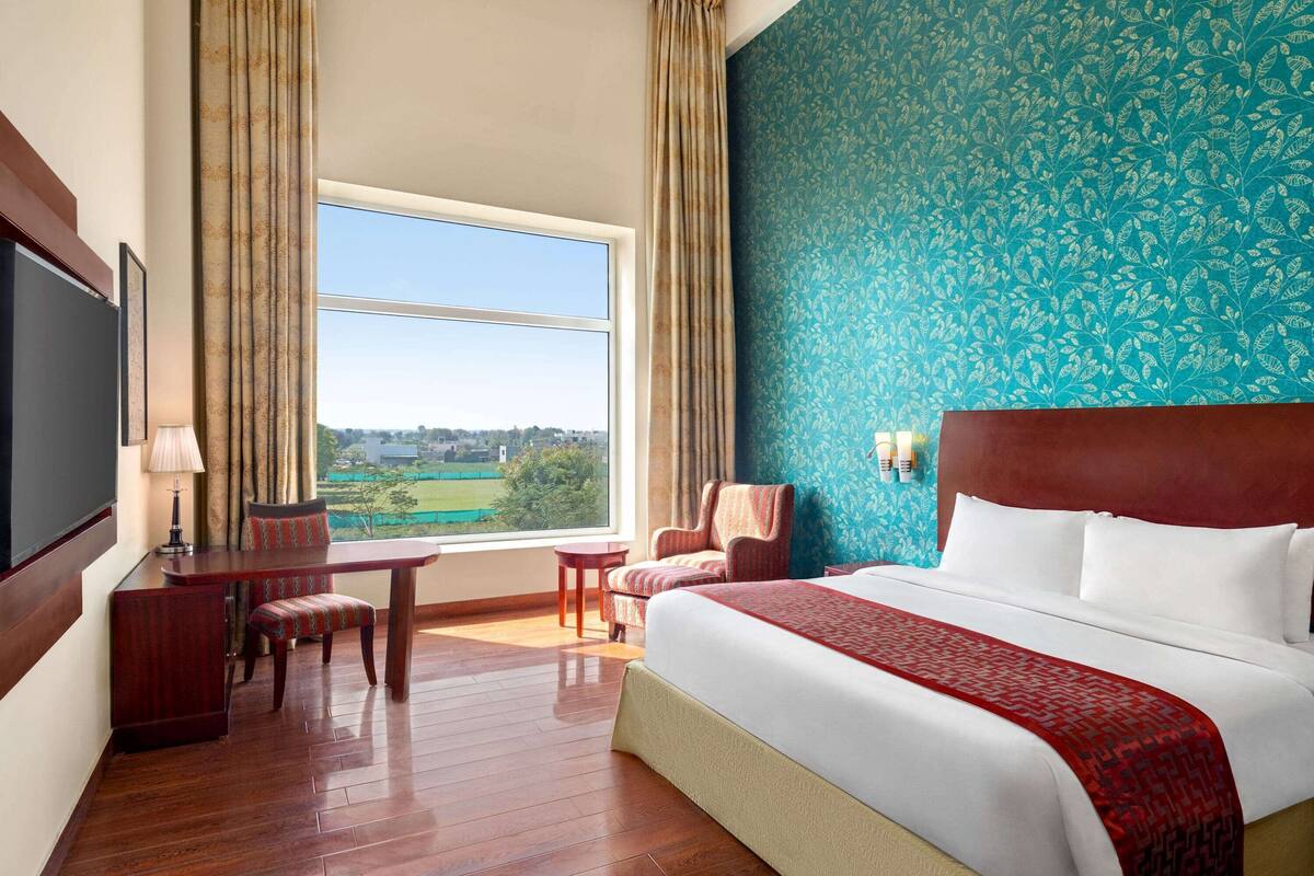A hotel room with a large bed, a desk, a chair, and a view of the outdoors.