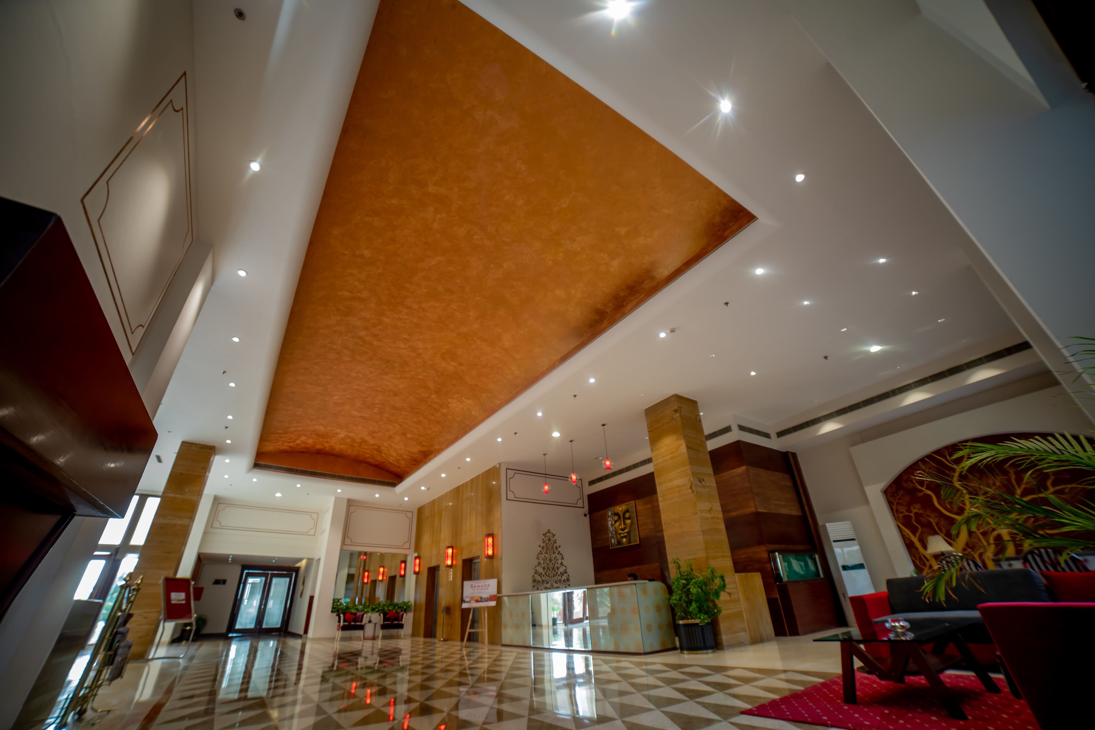 Um hall amplo com piso xadrez, balcão de recepção e uma grande parede decorativa.