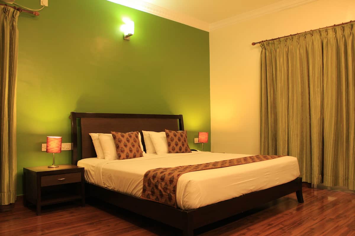 A neatly made bed with a patterned throw, a nightstand with a lamp, and a green wall.