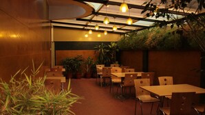 A restaurant with indoor seating, potted plants, and hanging pendant lights. - Hotel Trinity Suites (Bengaluru)