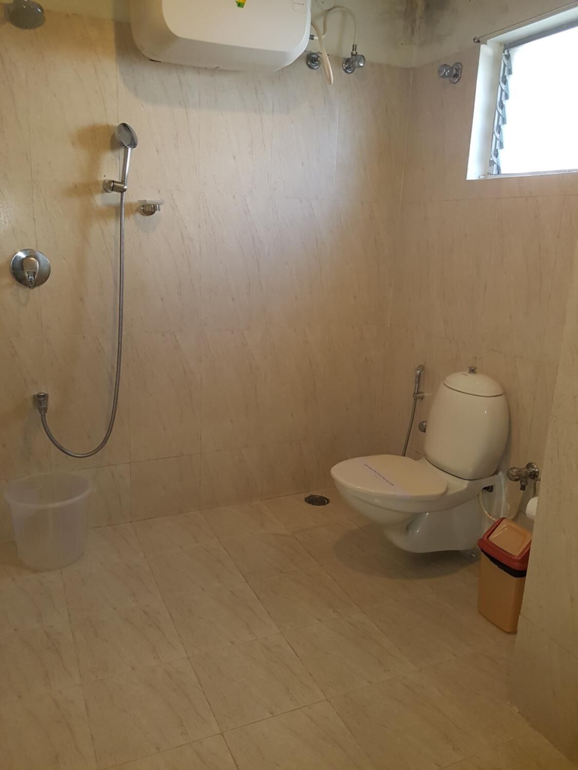 Une petite salle de bain carrelée, équipée de toilettes, d’une douche et d’une poubelle.