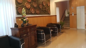 A lobby with a wooden reception desk, black leather chairs, and a large wall mural. - Hotel Trinity Suites (Bengaluru)