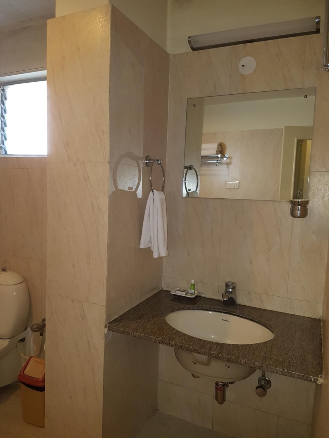 Un baño con lavamanos, espejo, toallero y retrete.