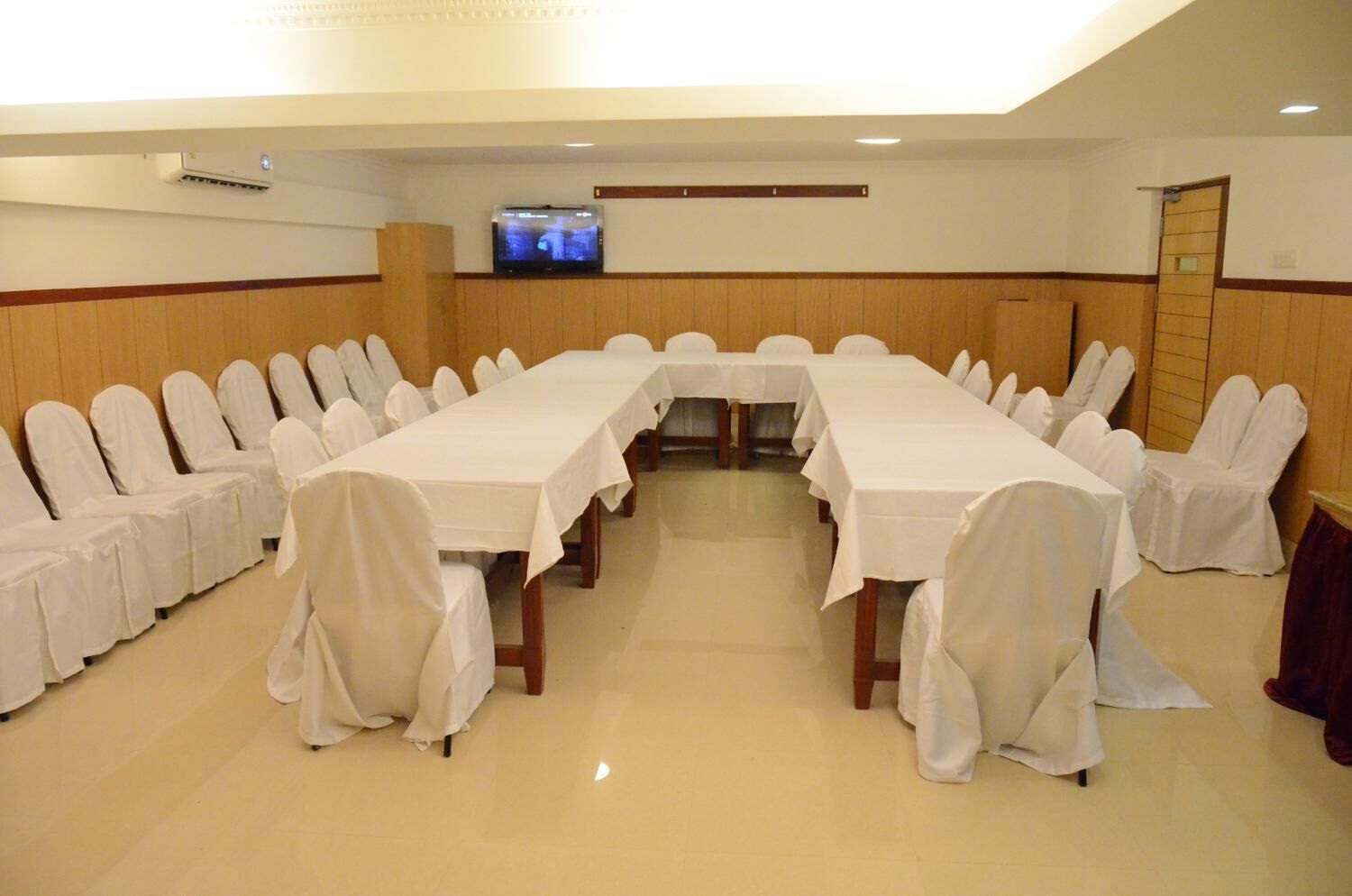 A conference room with a long table and chairs, a television on the wall, and a wooden panel design.