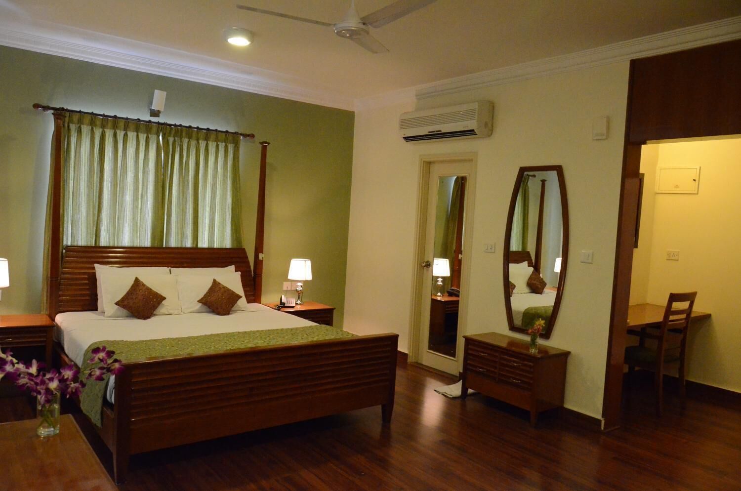 A hotel room with a wooden bed, bedside lamps, a mirror, a desk, and a chair.