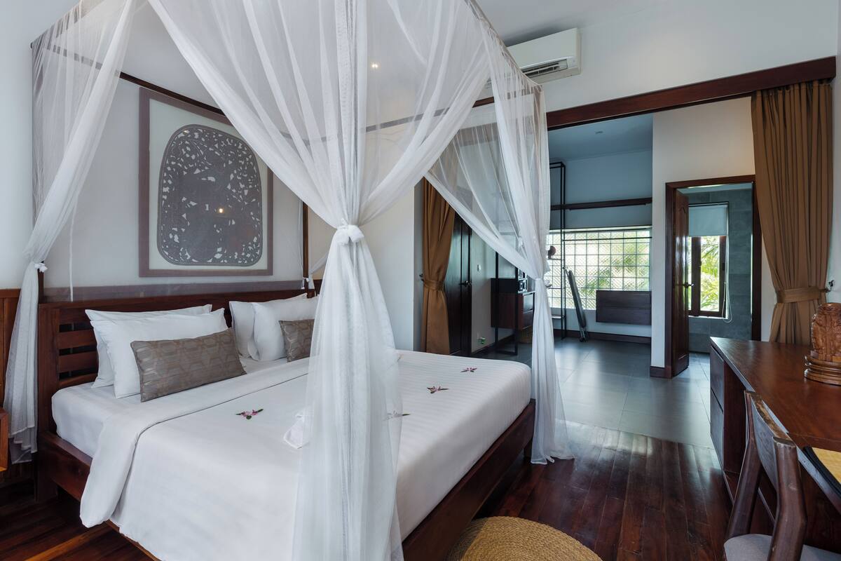 A bedroom with a four-poster bed, a large window, and a view of the outdoors.