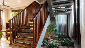 A wooden staircase with a handrail, leading to a landing area with a potted plant and a small table. - Golden Vishnu Villa (Siem Reap)