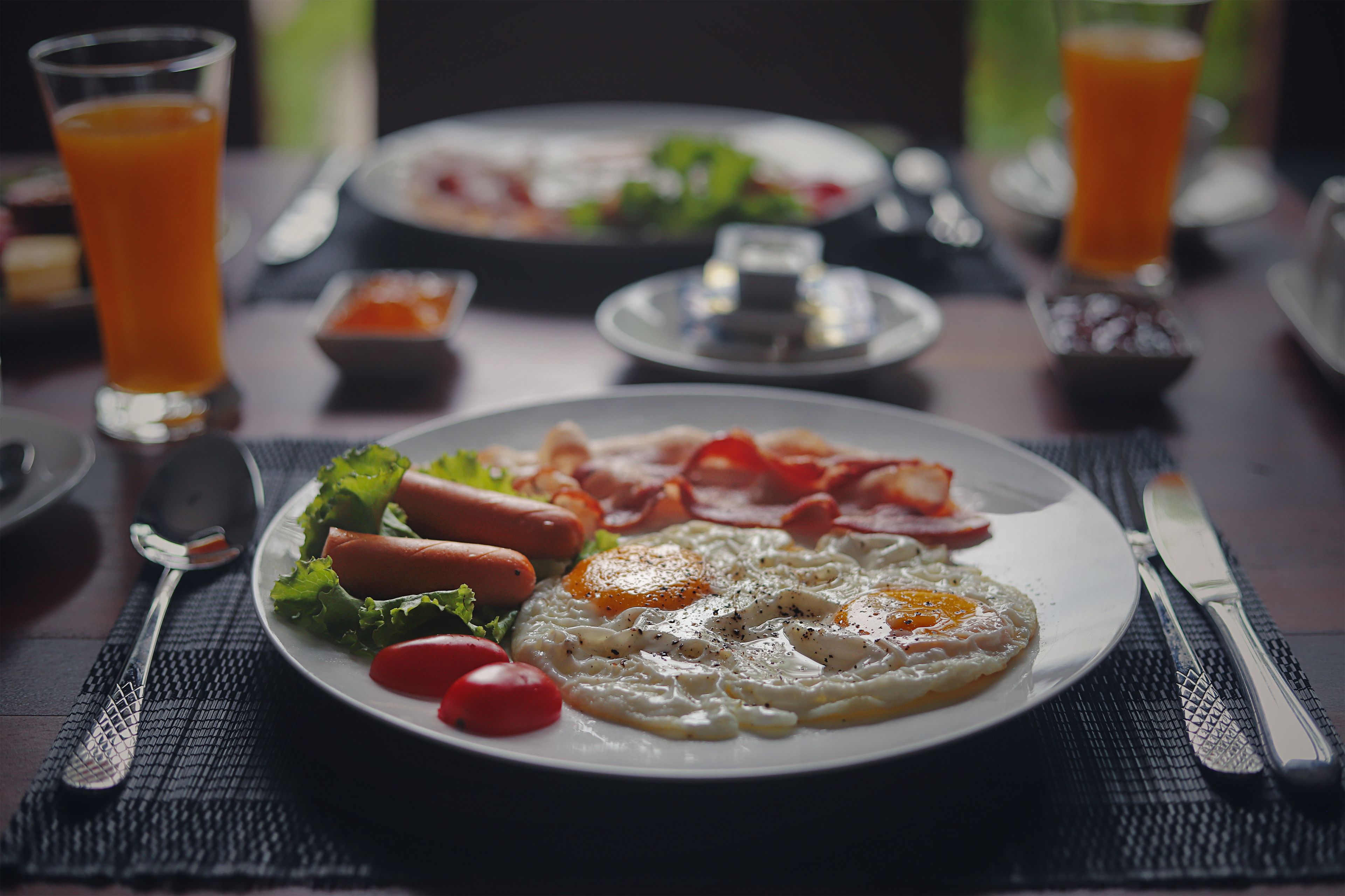 A breakfast plate with eggs, bacon, and tomatoes on a table with a fork and knife.