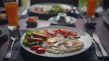 A breakfast plate with eggs, bacon, and tomatoes on a table with a fork and knife.